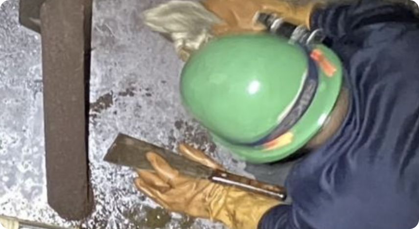 作業員が金属面を手作業で清掃・研磨している様子